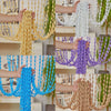 Hands are draping an elegant beaded string curtain with tassels in various colors like yellow, white, purple, blue, and beige