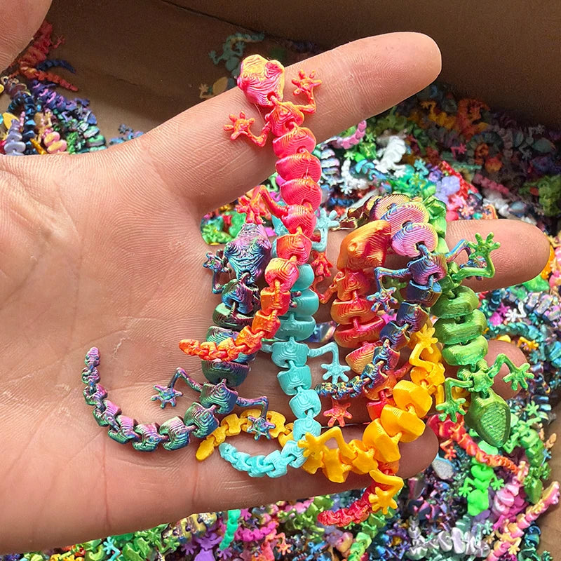 A hand holds a colorful 3D printed articulated gecko desk toy with vibrant scales and limbs.