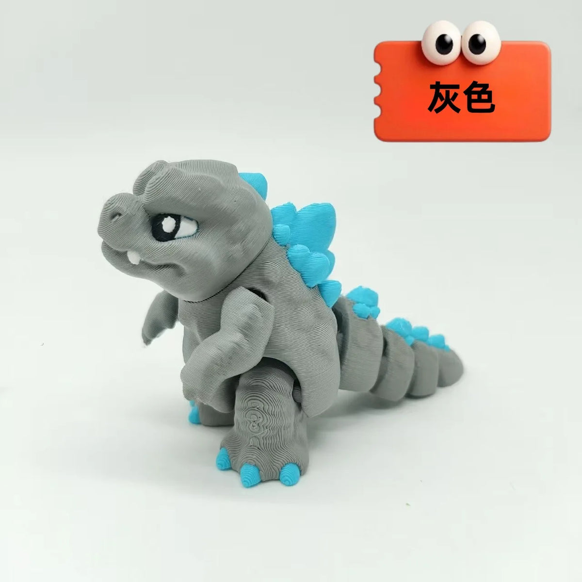 A gray 3D printed Godzilla sitting figure with blue accents is displayed next to an orange color swatch.