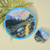 A round, handheld cooling fan featuring a landscape painting of mountains and a valley.