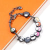 A silver charm bracelet featuring figures of Itadori, Fushiguro, and Gojo from Jujutsu Kaisen set against an orange backgroun