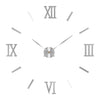 A silver-toned modern 3D acrylic wall clock face showing the Roman numerals XII, IX, III, and VI.