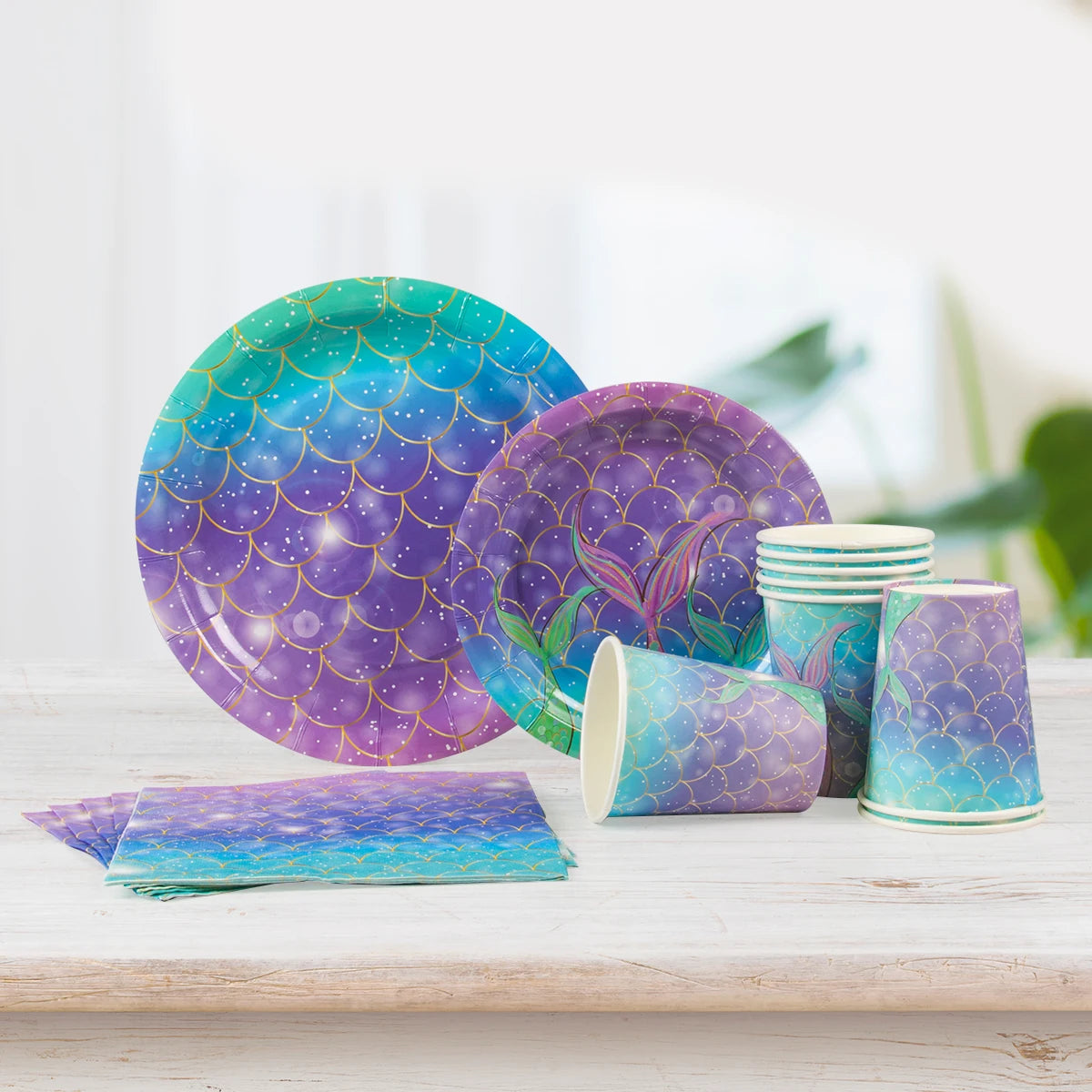 A purple and teal Under the Sea Mermaid Party tableware set featuring patterned plates, cups, and napkins on a wooden surface