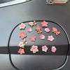 A collection of pink and orange 3D peach blossom flowers arranged on a dark car dashboard.