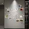 A gray wall decorated with white acrylic mirror tree decals and framed photos, featuring a family theme.