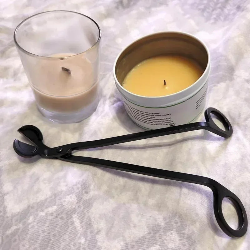 Stainless steel candle wick trimmer scissors resting on a white cloth next to a candle and a tin.