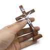 A handcrafted wooden crucifix with a figure of Christ is held in a person's hand.