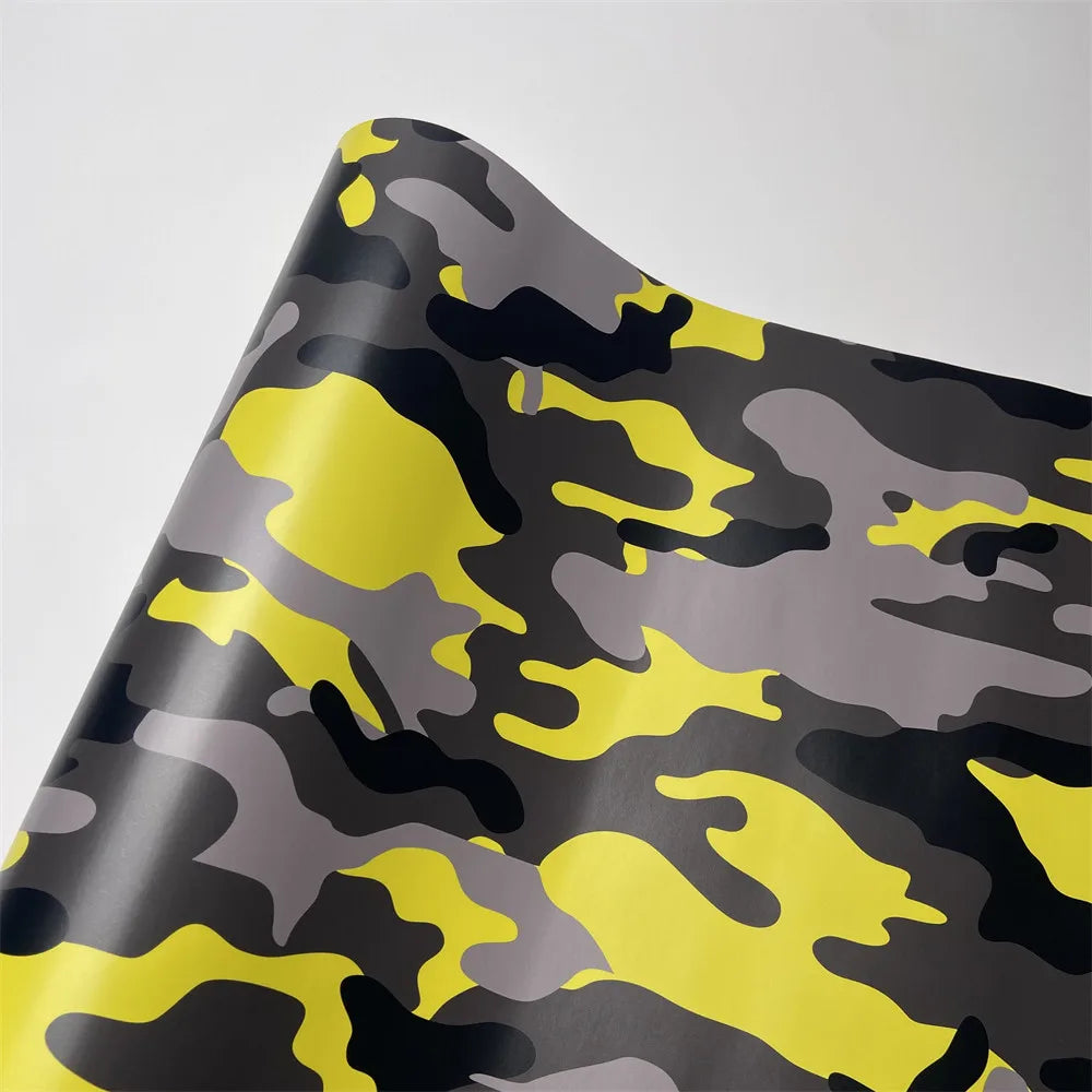 A close-up of color-changing digital camouflage vinyl wrap film showing shades of gray, black, and bright yellow.