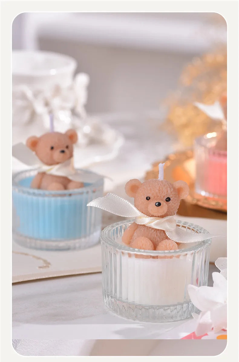 A soy wax teddy bear candle in a glass jar with a ribbon, set on a white surface.