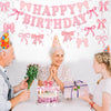 A woman is celebrating a birthday with a pink bow banner and cake, surrounded by two people.