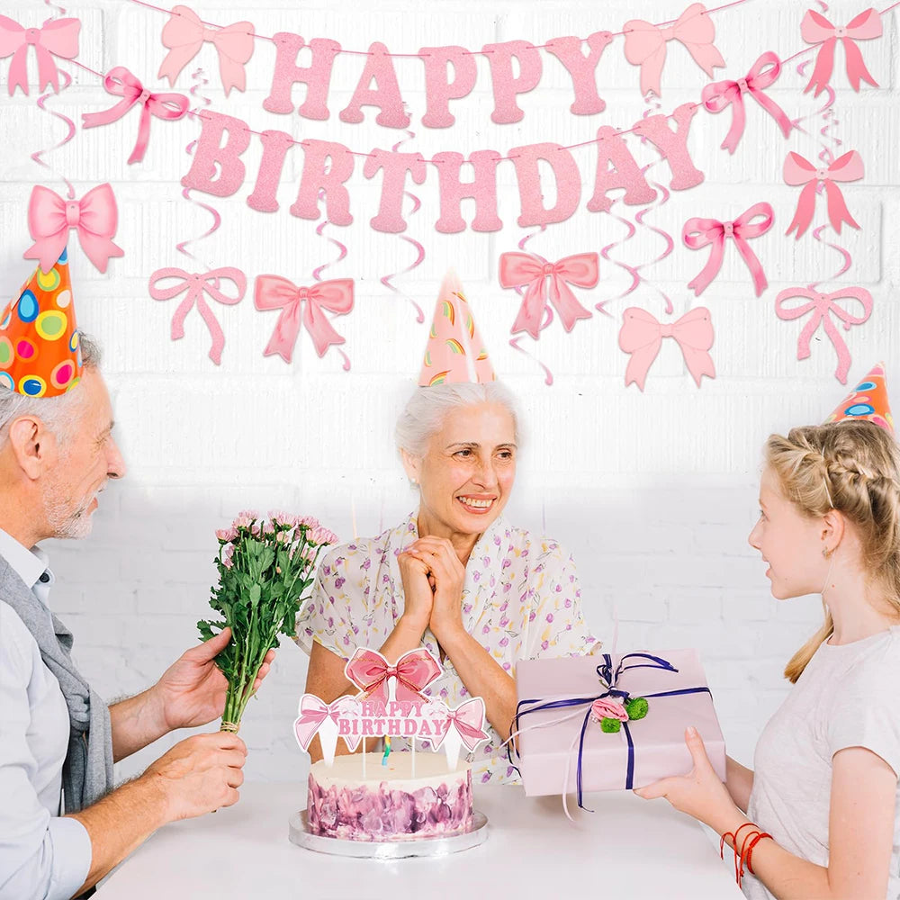 A woman is celebrating a birthday with a pink bow banner and cake, surrounded by two people.