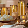 A collection of glowing amber glass pillar candles and small votives arranged on a wooden surface.