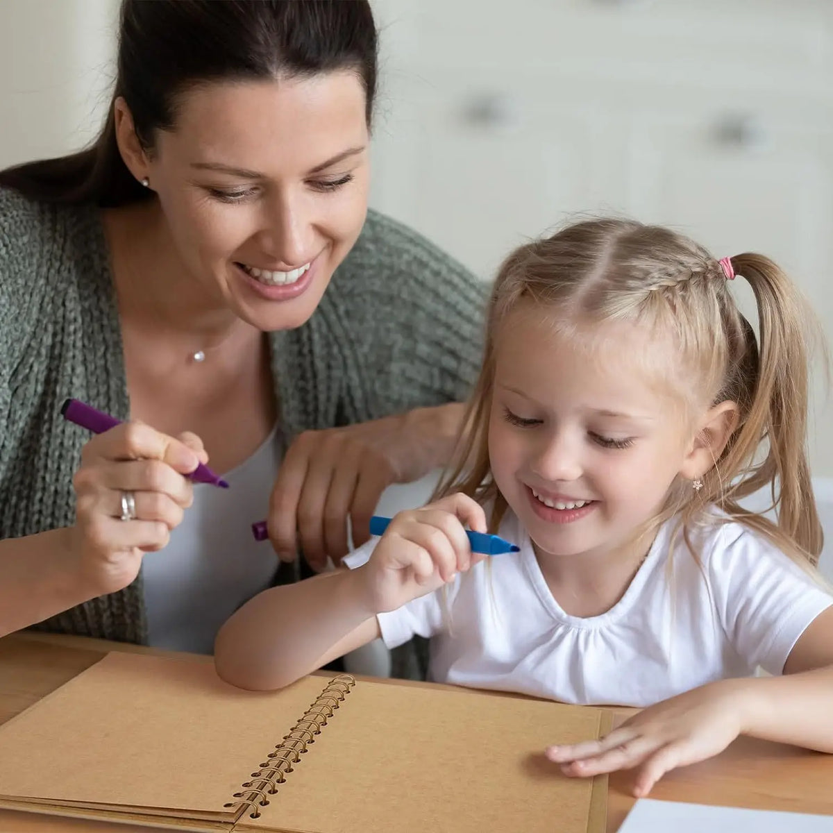 A woman is helping a young girl write in a brown scrapbook photo album.