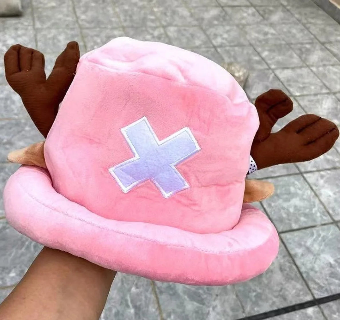 A pink knit cap plush toy resembling Tony Tony Chopper with brown ears and a white cross design
