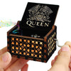 A carved wooden music box with a black lid featuring the word QUEEN and intricate wood carvings.