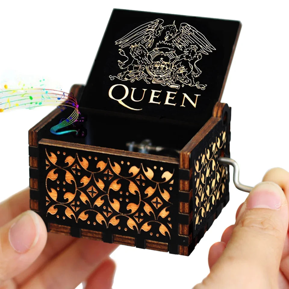 A carved wooden music box with a black lid featuring the word QUEEN and intricate wood carvings.