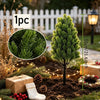 A single artificial pine tree with a dark trunk and green needles is shown in a garden setting for holiday decor.