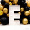 A large white marquee light-up letter E is displayed in front of a background of gold and black balloons.