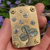 A small gold-toned metal press kit featuring embossed flowers and a large dried green and blue shamrock.