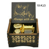A wooden box containing a gold-colored music box with an anime character design on the lid.