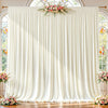 A white fabric backdrop with vertical pleats and floral greenery hangs between arched windows.