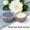 White tea floral aroma candle surrounded by white roses and green leaves on a denim background