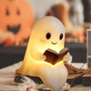 A cute ghost figurine lamp with a warm glow is shown resting on a wooden surface.