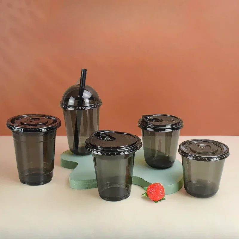 A collection of black disposable U-shaped coffee cups on a light surface with a small red fruit.