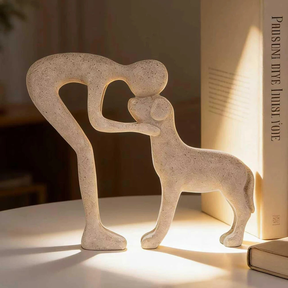 A light beige sculpture depicting a human and a dog embracing, carved from stone or ceramic.