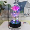 A glass dome containing a pink rose with glowing filaments and LED light, resting on a black base.