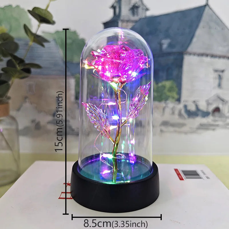 A glass dome containing a pink rose with glowing filaments and LED light, resting on a black base.