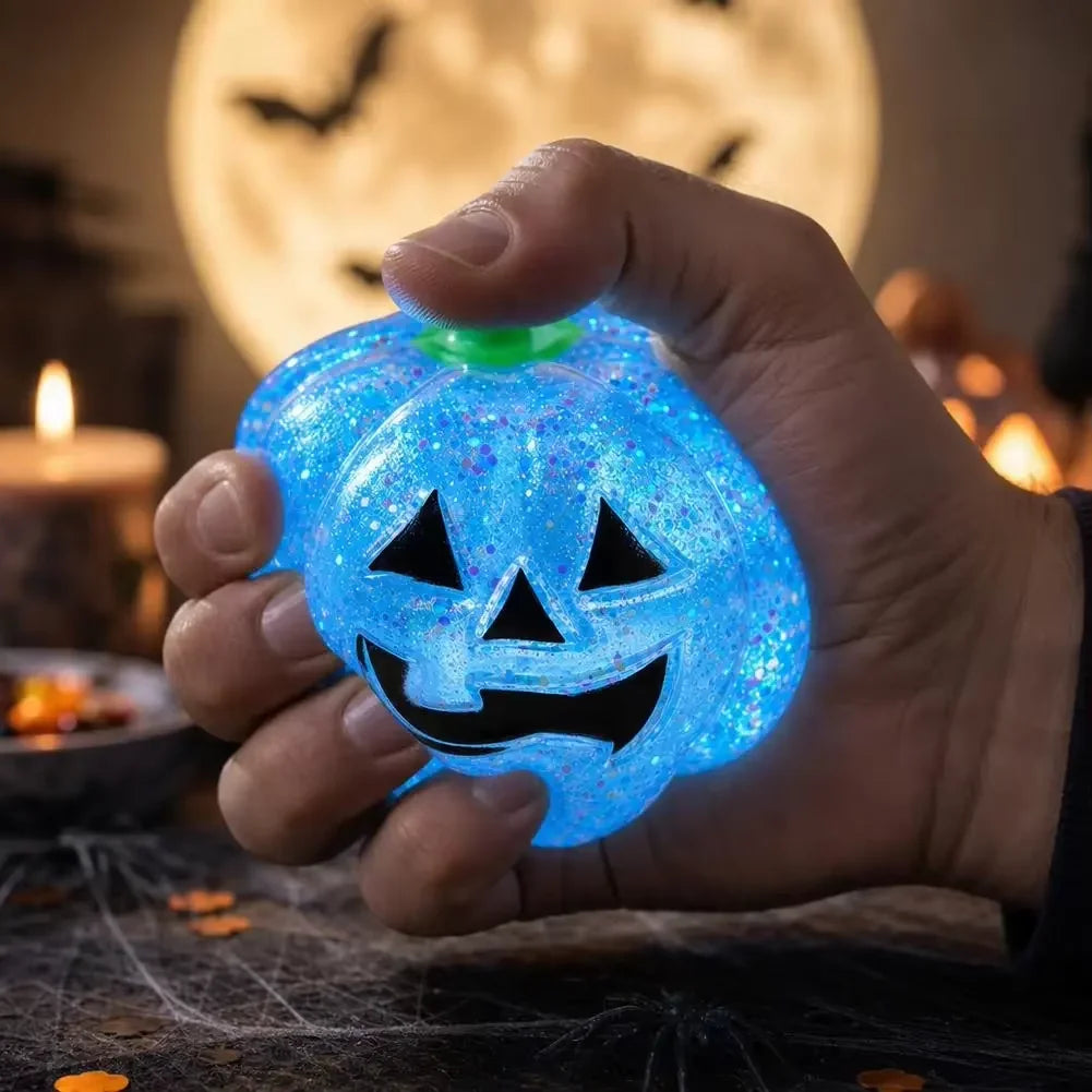 A hand holds a glowing blue Halloween pumpkin stress ball with a carved face against a dark background.