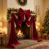 A velvet Christmas tree bow with long draping tails displayed on a fireplace mantel decorated with greenery.