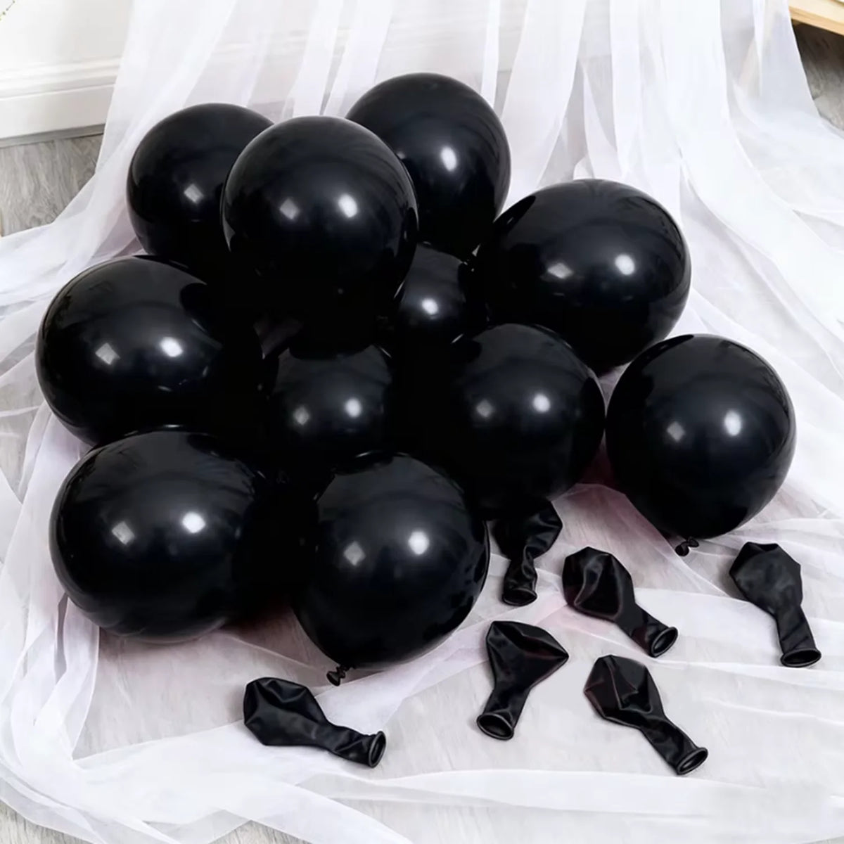 A collection of glossy black latex balloons and black balloon ties displayed on white sheer fabric.