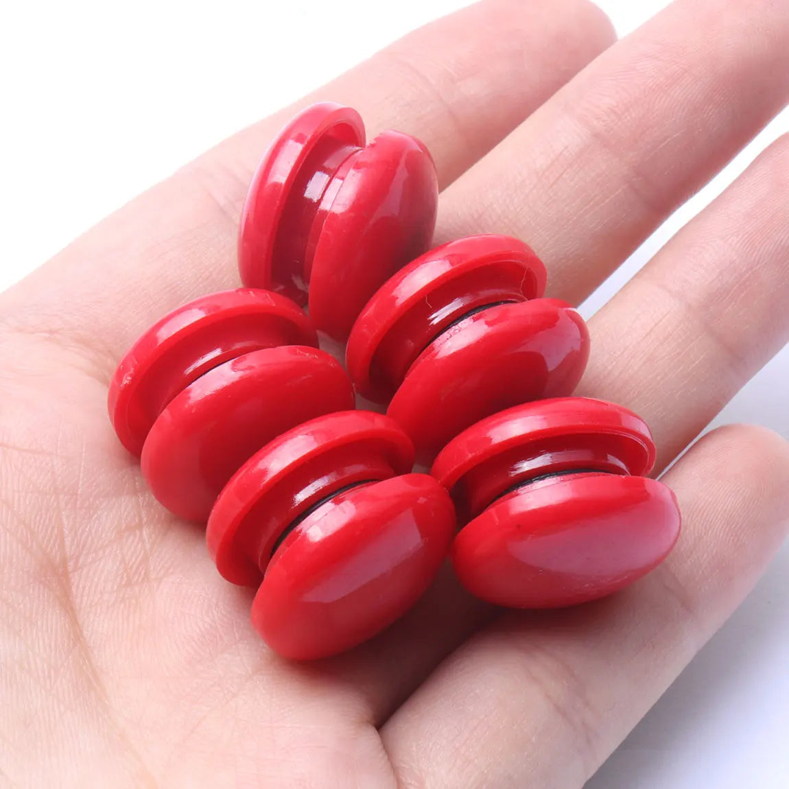 A hand holds a set of ten bright red, oval refrigerator magnets.
