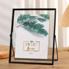 A black photo frame displays a green tropical leaf design with the text Sweet home on a white background.
