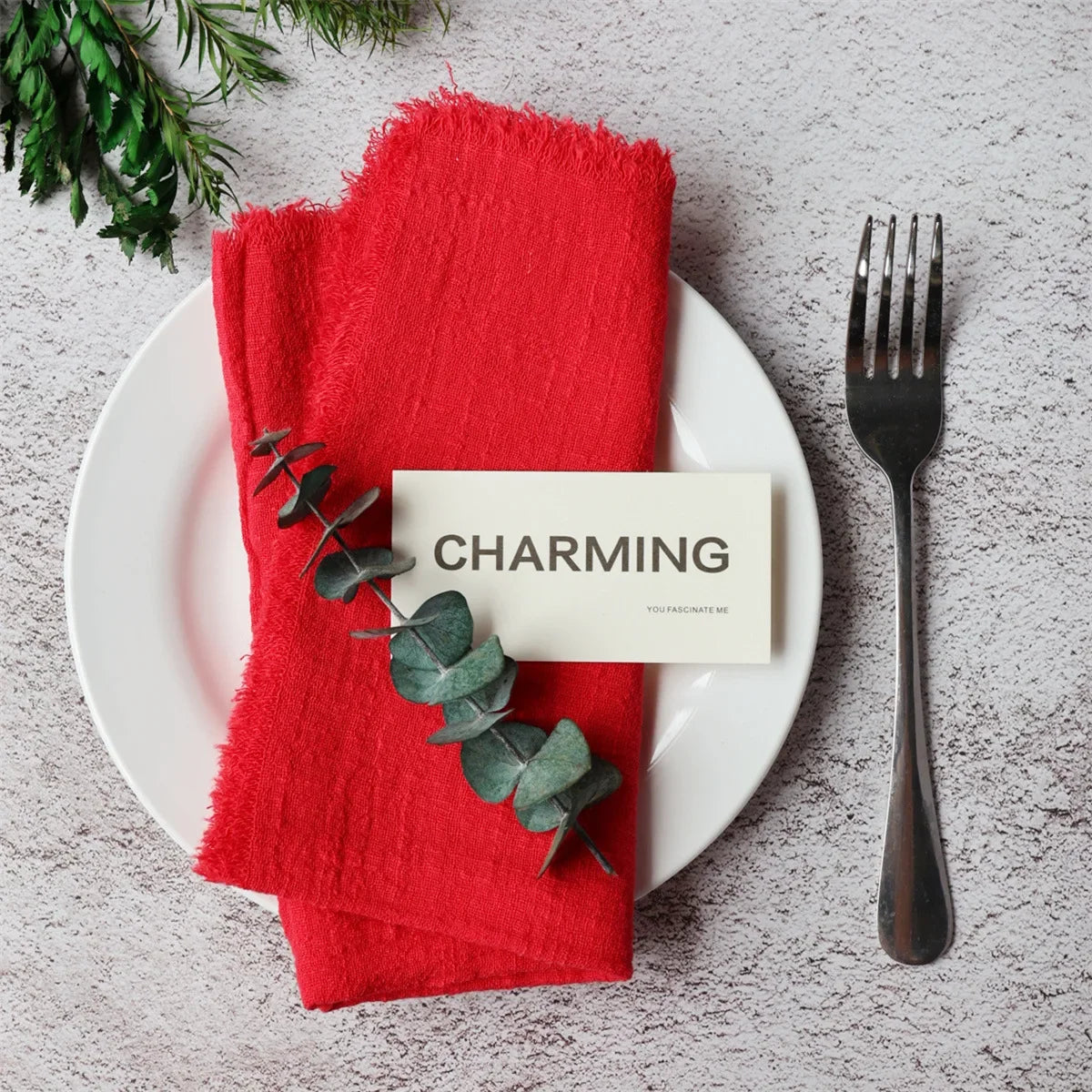 A red folded napkin with green leaves rests on a white plate next to a black fork.