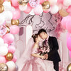 A bride and groom pose in a pink and gold balloon decorated setting with pink floral arrangements.