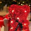 Ein Strauß leuchtend roter künstlicher Rosen, zusammengebunden, neben einer verpackten Geschenkbox.