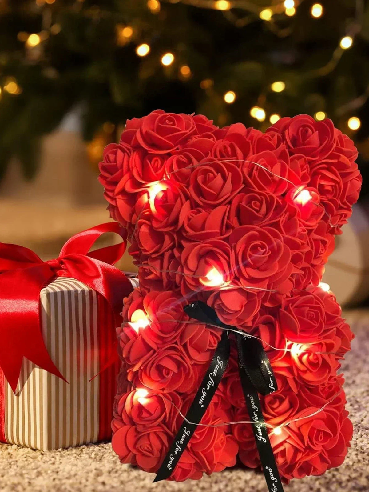 Ein Strauß leuchtend roter künstlicher Rosen, zusammengebunden, neben einer verpackten Geschenkbox.