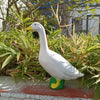 A white goose garden statue with a green base is shown amidst green foliage.