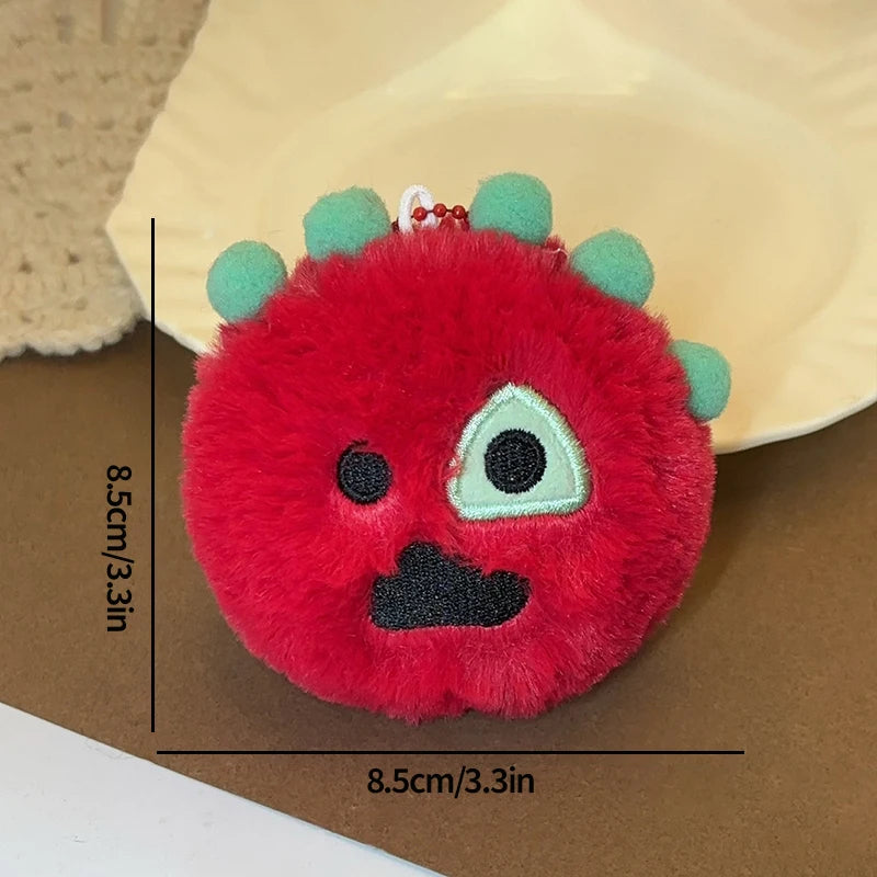 A round, bright red plush toy with green accents and a clear plastic holder attached, shown against a brown surface.