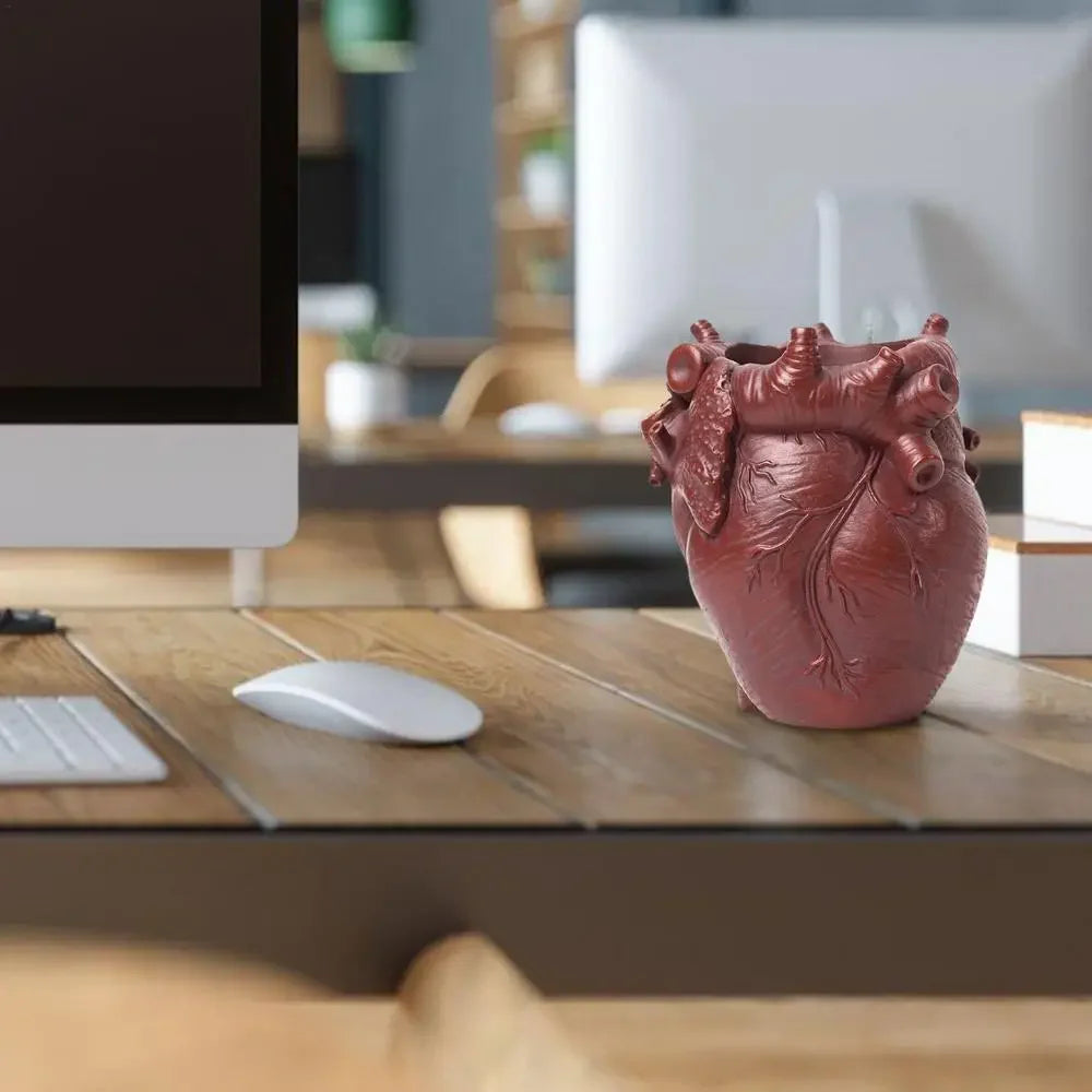 A reddish-brown heart-shaped resin pen organizer sits on a wooden desk next to a computer monitor and a white mouse.
