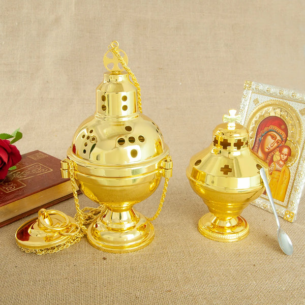 A gold-plated Orthodox censer with bells displayed on a beige cloth next to a religious icon.