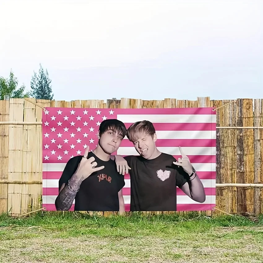 A pink American flag tapestry featuring stars and stripes displayed outdoors against a wooden fence.