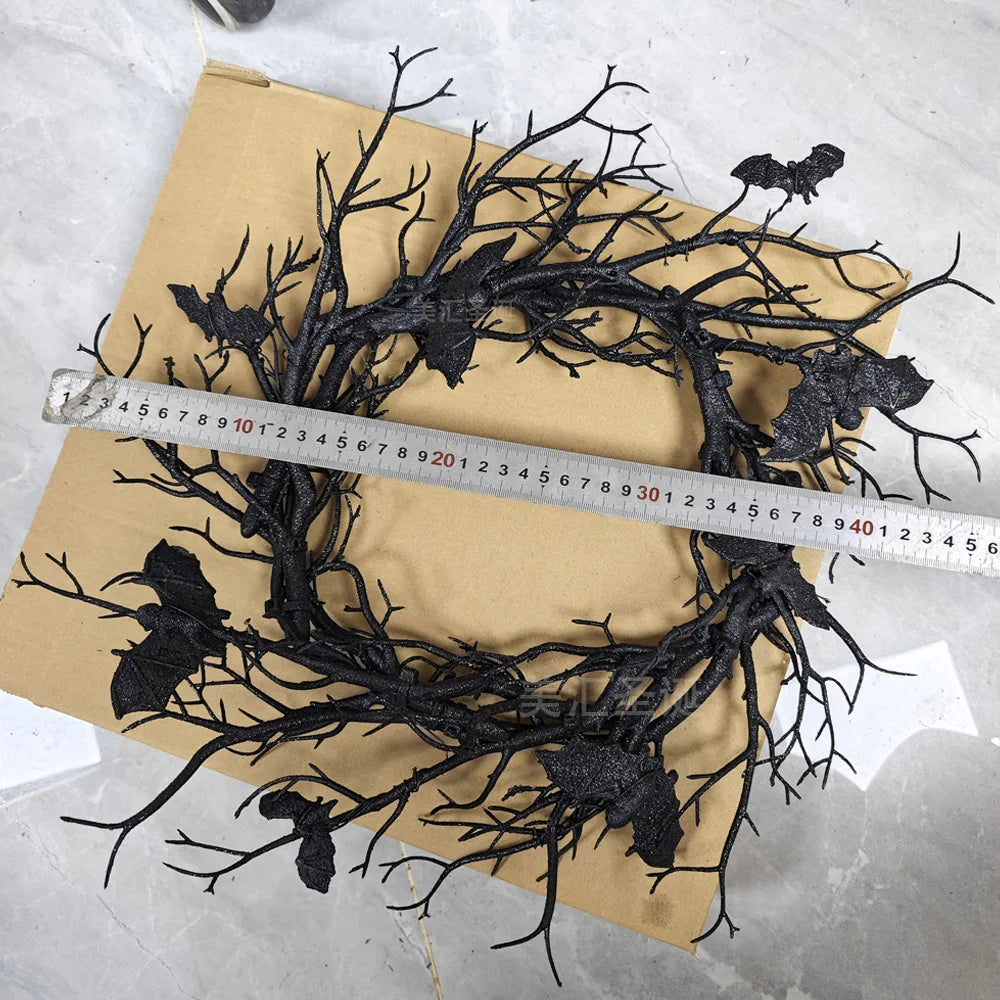 An artificial black branch bat wreath for Halloween door decor is laid out on brown paper next to a ruler.