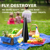 A black electric fly destroyer fan is shown above a picnic blanket with fruit and treats in a grassy outdoor setting.
