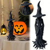 Estatua de bruja gótica gris oscura con sombrero ancho y túnicas fluidas, junto a una calabaza naranja.