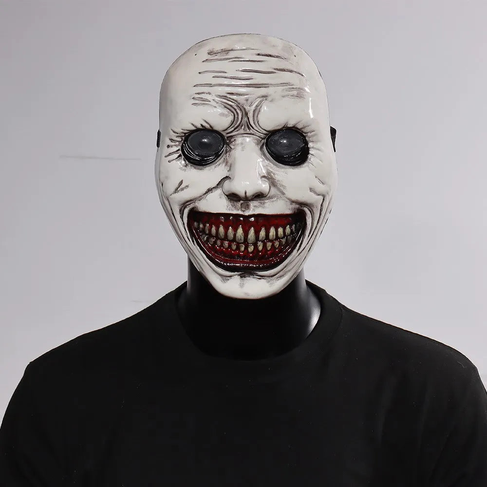 A white demon mask with a wide, menacing grin and red teeth displayed on a black mannequin.