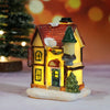 A miniature festive Christmas house with a tiled roof and warm LED light glow, resting on a snowy base.